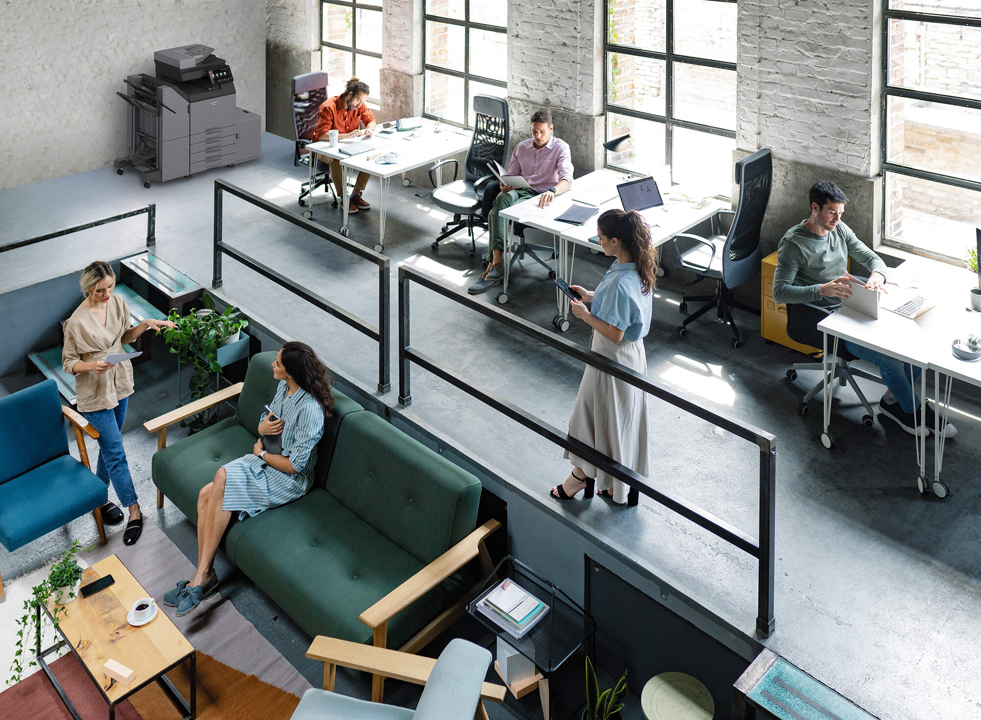 Wide Angle View of a Modern Loft Open Space Office With Businesspeople Working in It Open-plan loft office with multiple people working at desks by large windows; a copier on the left, and a lounge area with plants in the foreground.