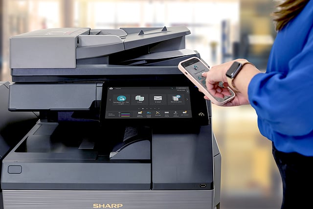 Copier Lease Services Included: What’s Covered Person in a blue sleeve uses a smartphone to print wirelessly from a Sharp multifunction printer.