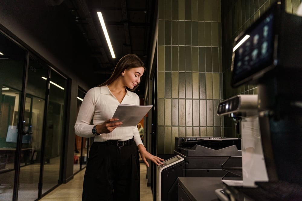 Lease a Copier Steps for a Smooth Service A woman in a jacket is printing on a printer, an employee in a specialist copywriter company. A confident person works in a coworking space. Smart freelancer startup project.