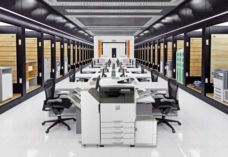 Cost of Unmanaged Printing: Reduce Expenses with Sharp MFPs-Sharp-Section-2 Open-plan office with long rows of desks and chairs, flanked by wall-to-wall server racks; a large central printer/copier.