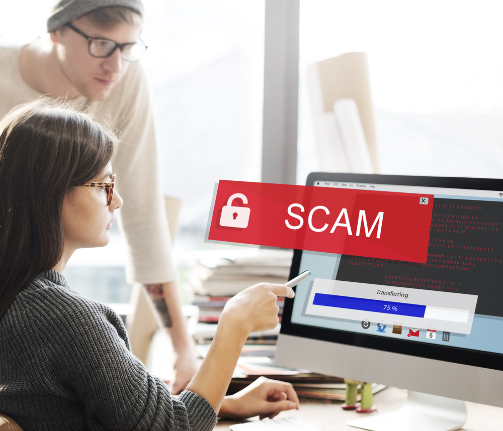 UCC Filing Solicitation Scams: Avoid Fraud in Texas Two people sit at a desk, a red 'SCAM' warning banner with a lock icon covers a computer screen to indicate online fraud risk.