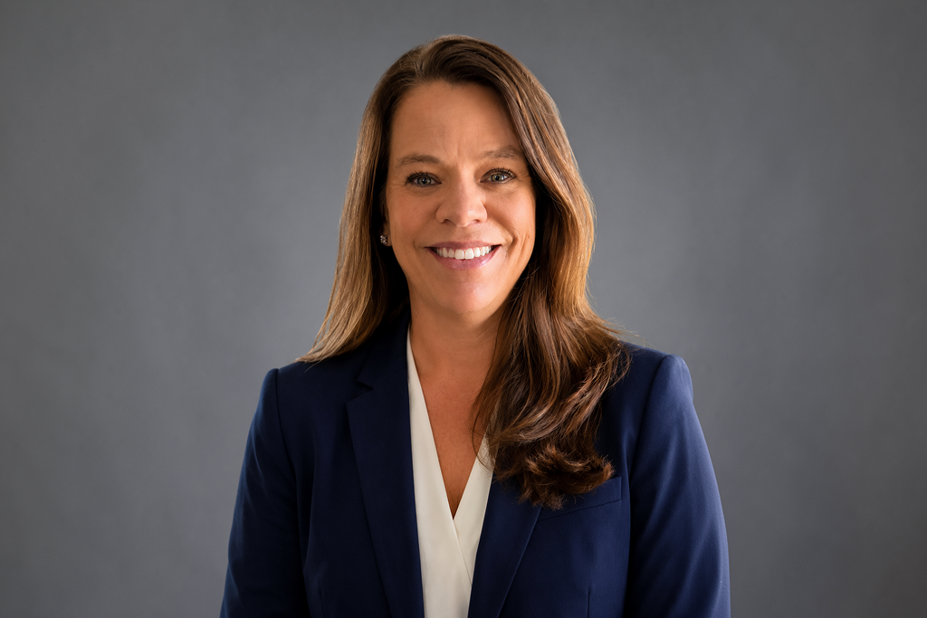 Professional Headshot of a Woman in a Navy Blazer and White Blouse Smiling at the Camera Against a Gray Backdrop