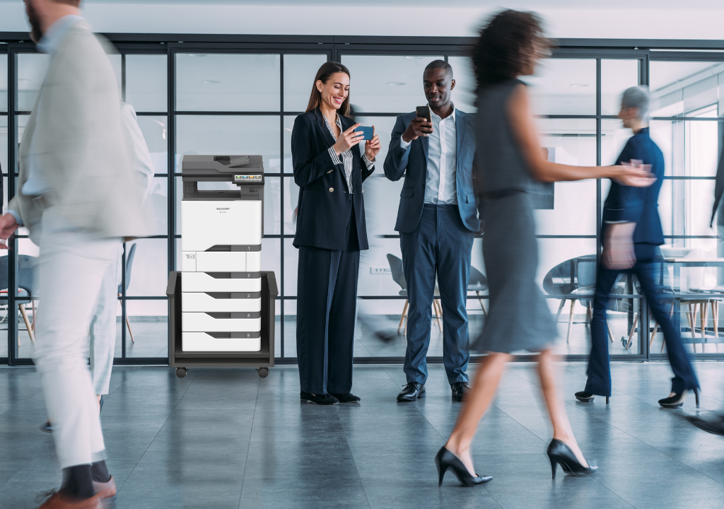 Print Service Implementation: A Step-by-Step Guide Two professionals pause in a modern office lobby to check their phones beside a wheeled copier cart by glass-walled offices?