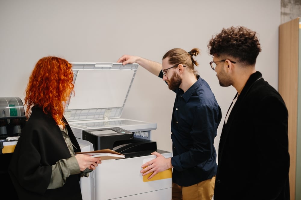 What Is Included in Managed Print Services? (2026 Guide) Diverse business people working together, handling reports and using an office multifunction printer for document reproduction